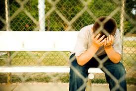 Sad boy sitting on a park bench behind a chainlink fence